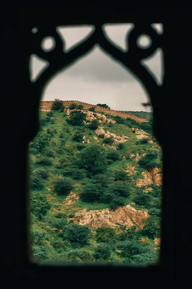 View of green hills and stone walls framed through an arched Moroccan-style window.