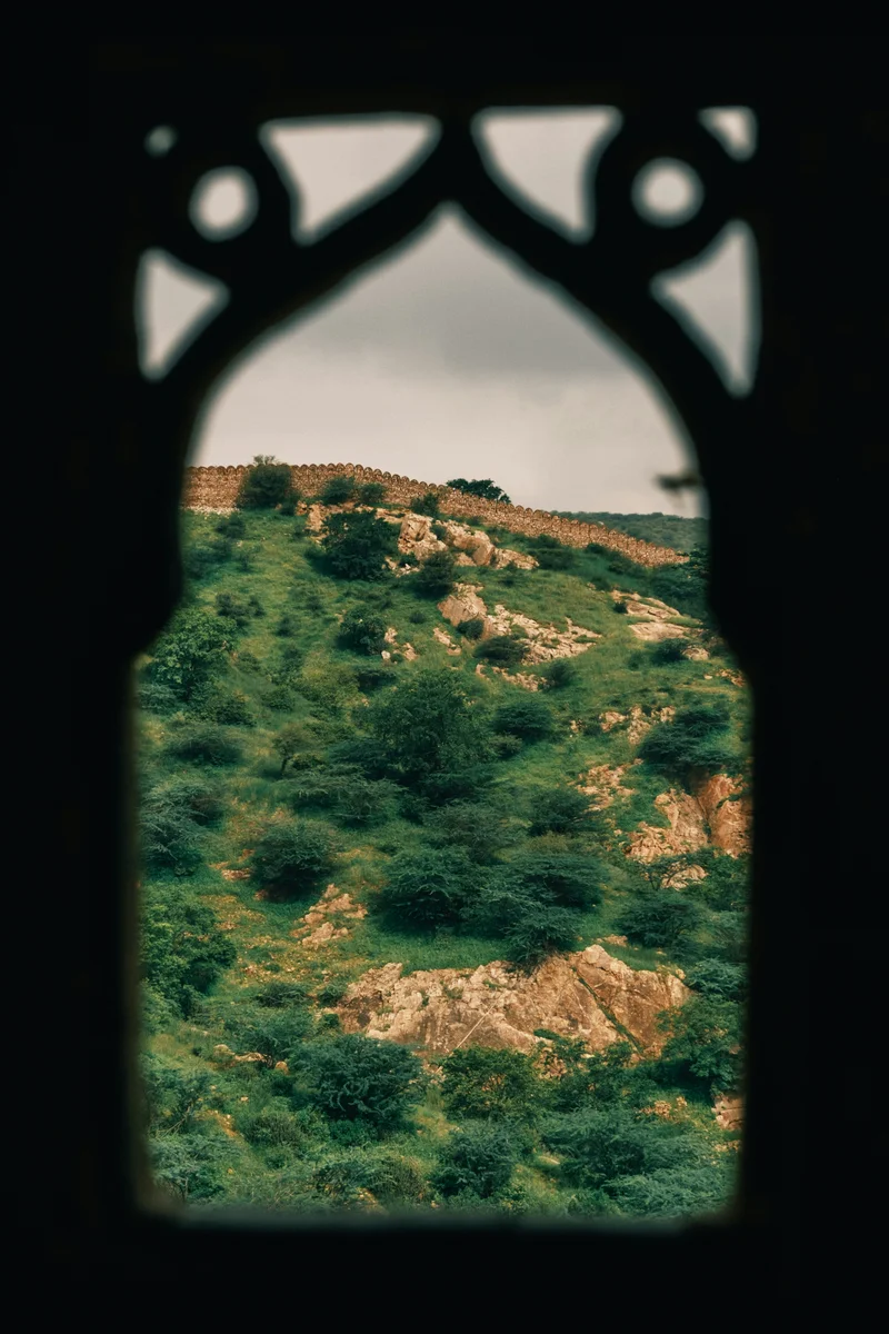 View of green hills and stone walls framed through an arched Moroccan-style window.