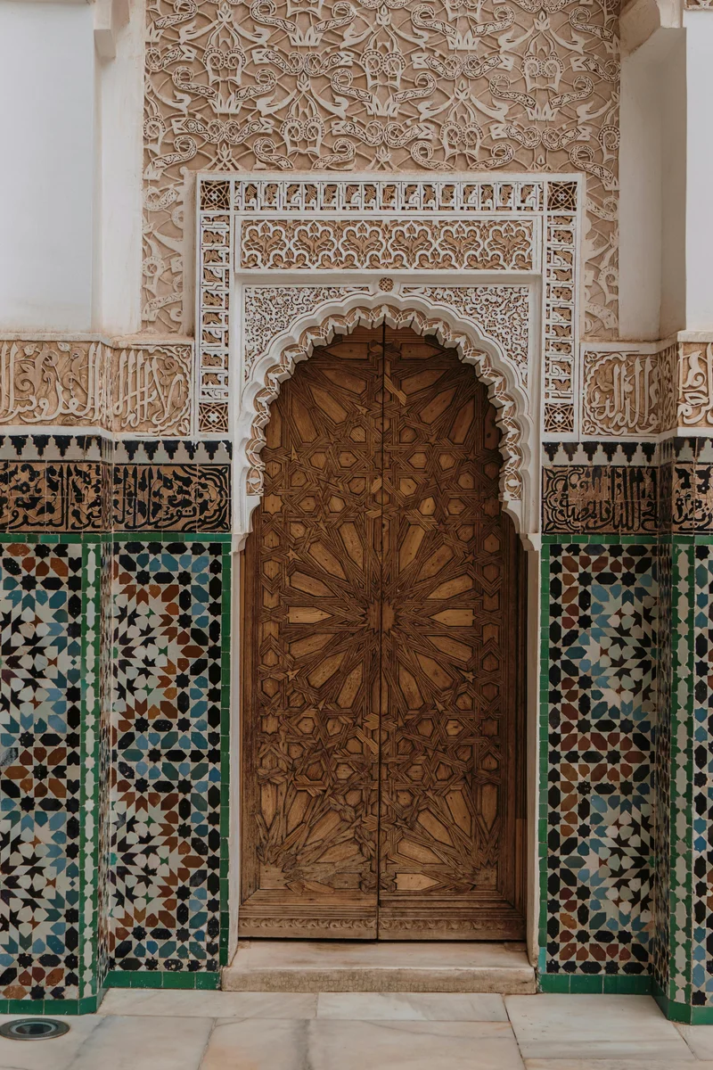 Close-up of carved wooden door surrounded by zellige tiles at Ben Youssef Madrasa.