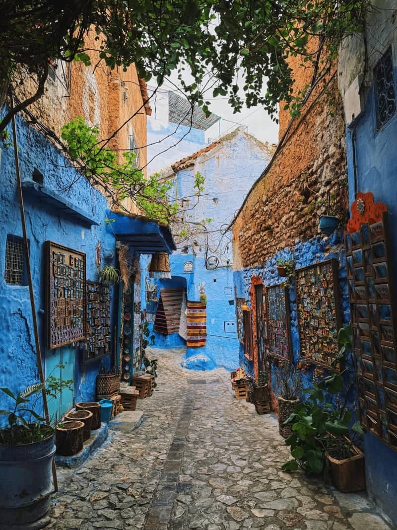 Narrow blue alley in Chefchaouen lined with shops selling handicrafts and textiles.