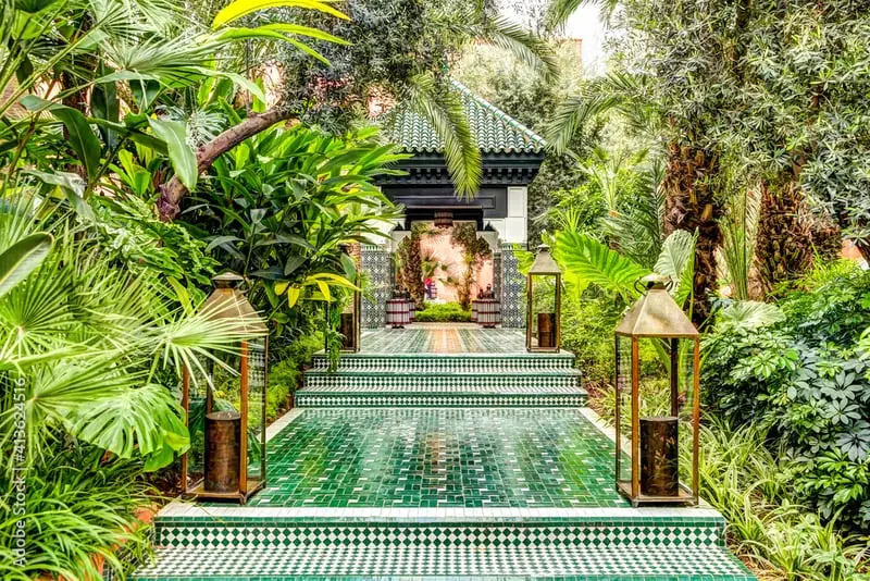 Lush garden with green zellige-tiled steps and lanterns leading to a riad pavilion.