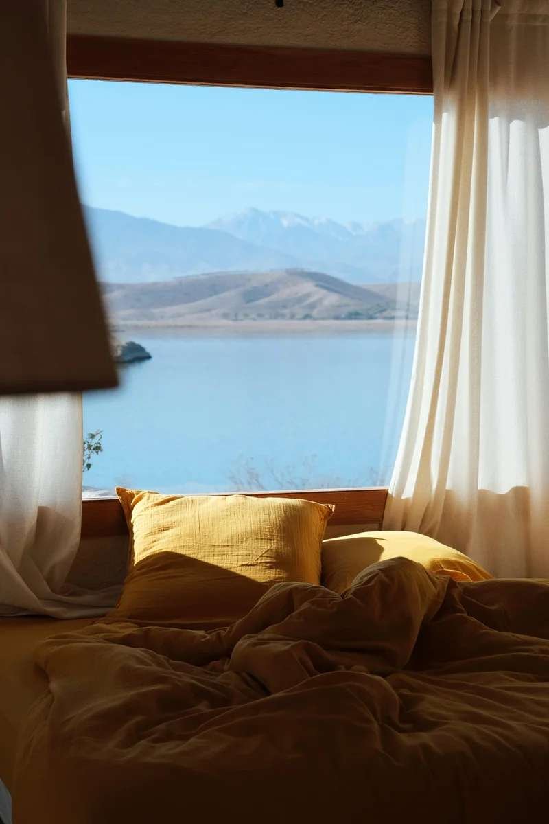 Romantic mountain lodge bedroom overlooking Atlas Mountains and lake through sheer curtains