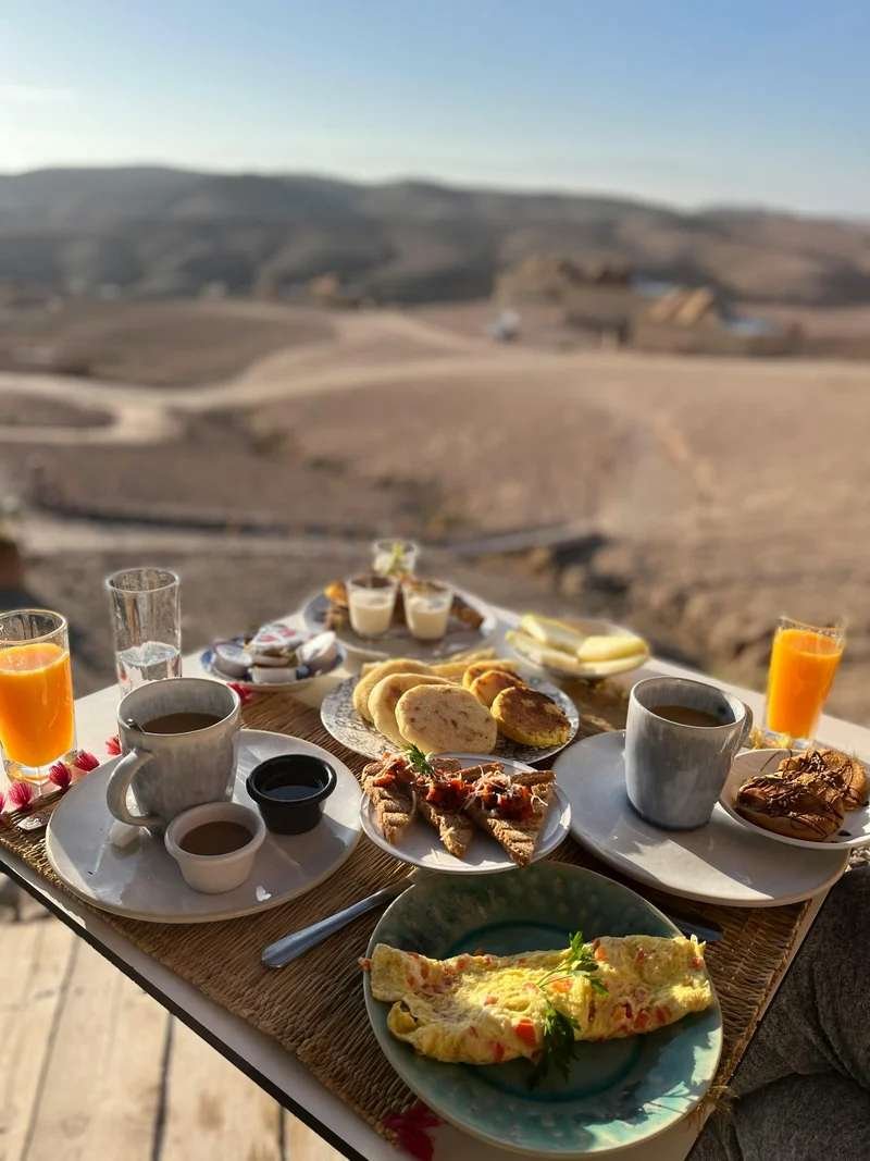 Romantic luxury breakfast setup with Moroccan pastries and tea overlooking dramatic desert landscape, embodying the intimate Morocco honeymoon experience