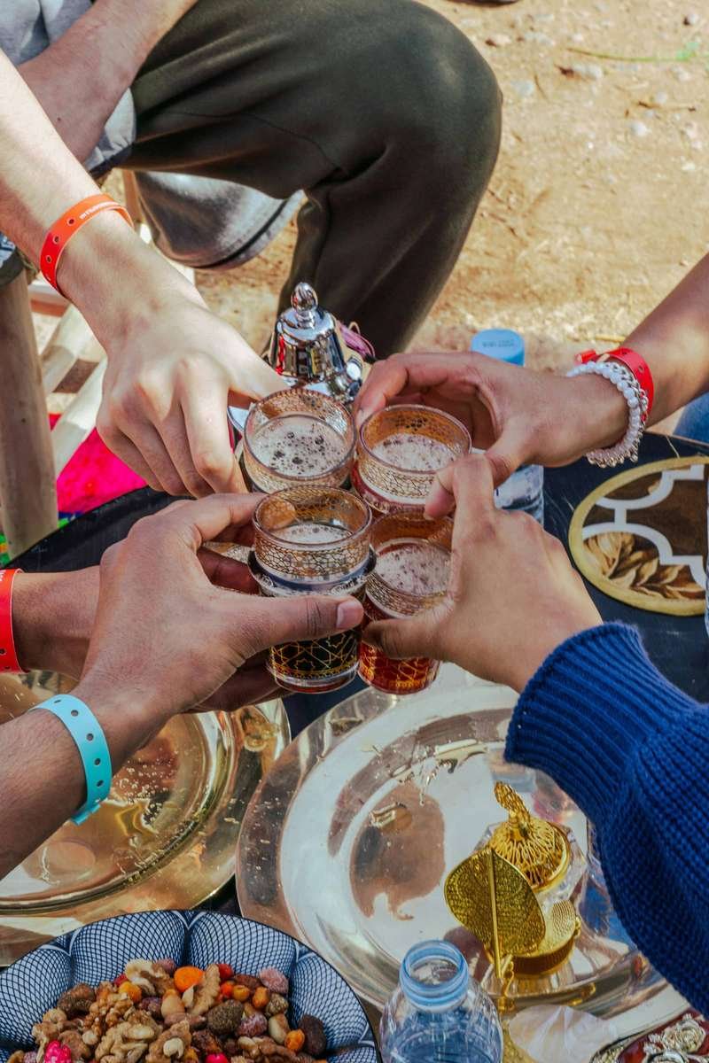Hands raising traditional Moroccan mint tea glasses in a toast, symbolizing the hospitality and relationship-building central to Moroccan culture and accommodation partnerships