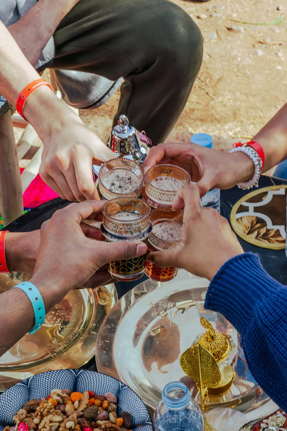 Hands raising traditional Moroccan mint tea glasses in a toast, symbolizing the hospitality and relationship-building central to Moroccan culture and accommodation partnerships