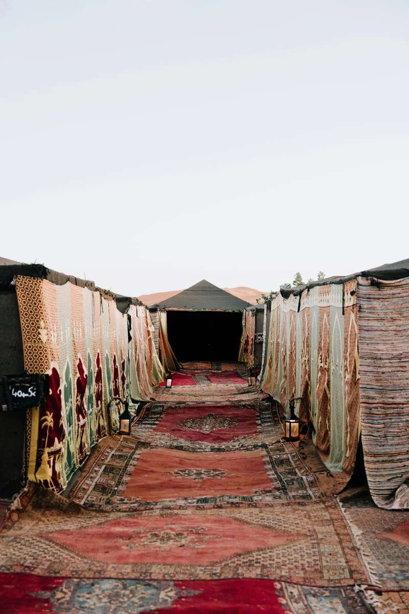 Traditional Moroccan carpet path leading to luxury desert tents at twilight
