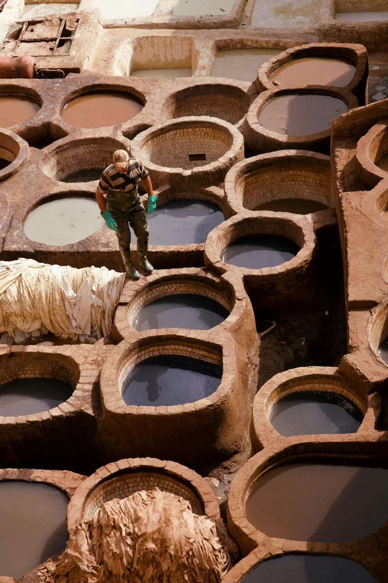 Worker at Fes' Chouara Tannery among colorful circular dye pits showing the city's authentic craft traditions and working medieval industries.