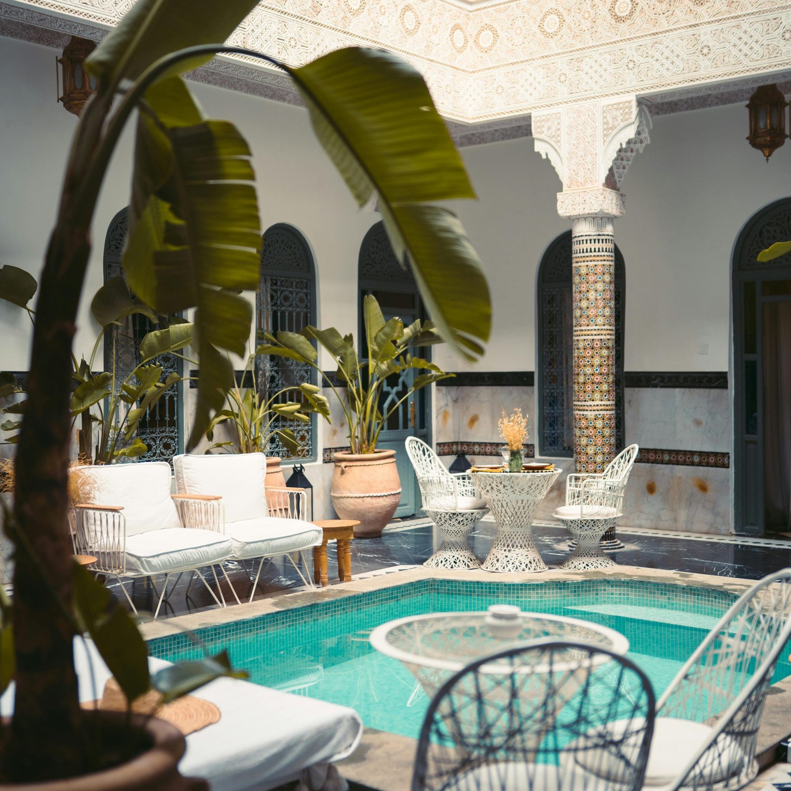Elegant central courtyard of a luxury Marrakesh riad featuring a serene swimming pool surrounded by intricate traditional Moroccan zellige tilework.